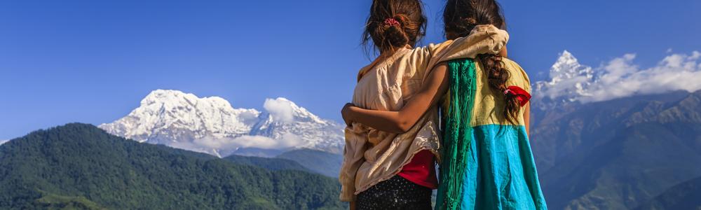 Two girls holding eachother while looking out over mountains in Nepal