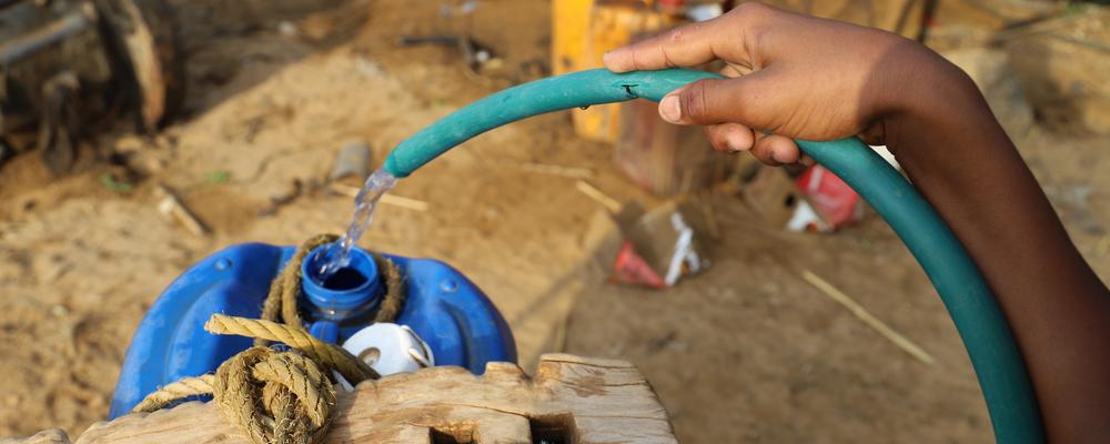 Person holding a water hose to fill a flask with water